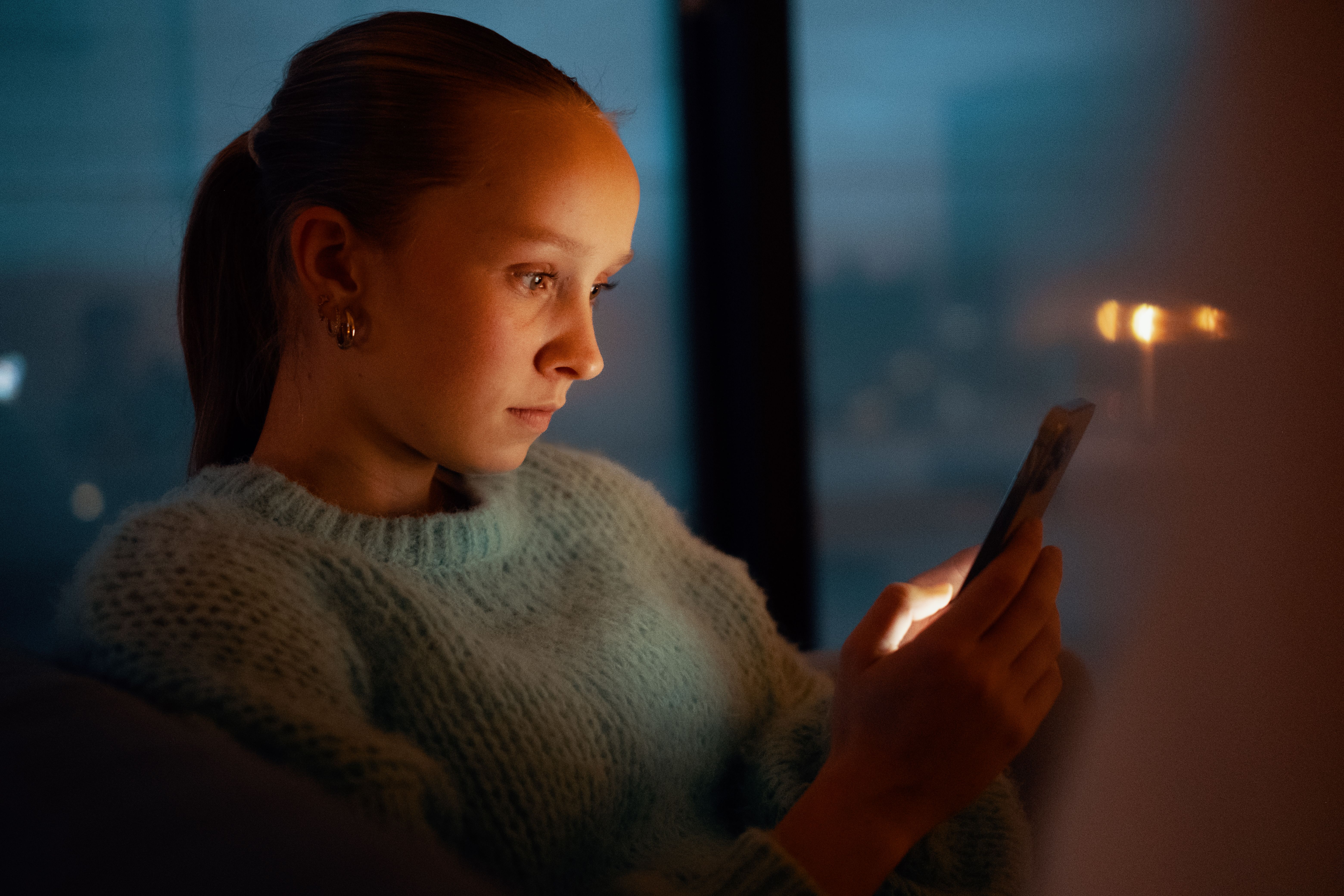Jente som leser på mobilen i mørket