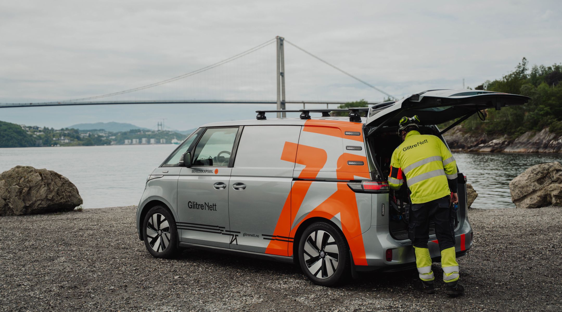 Energimontør med arbeidsbil foran hav og bro