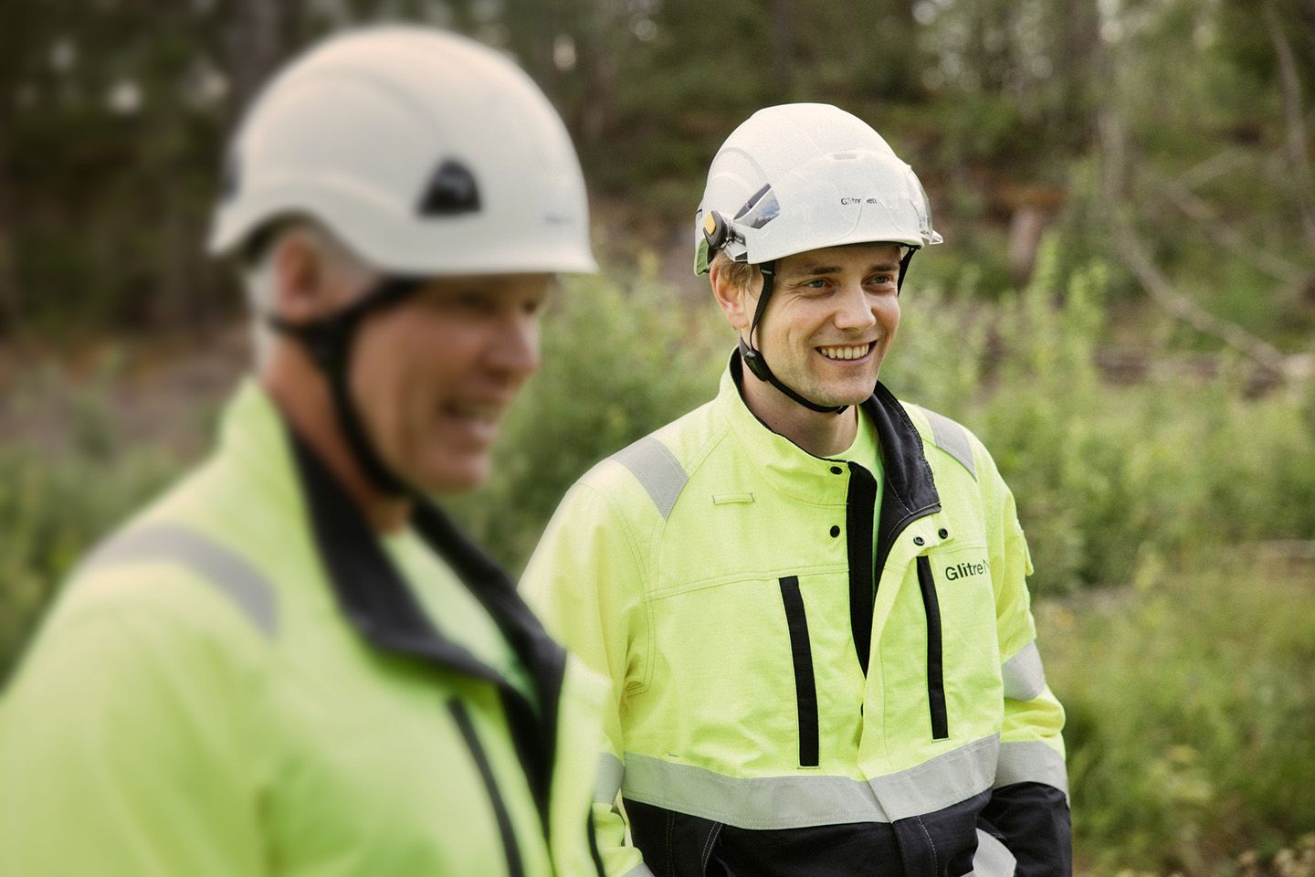 To menn med arbeidstøy og hjelm. skog i bakgrunn.