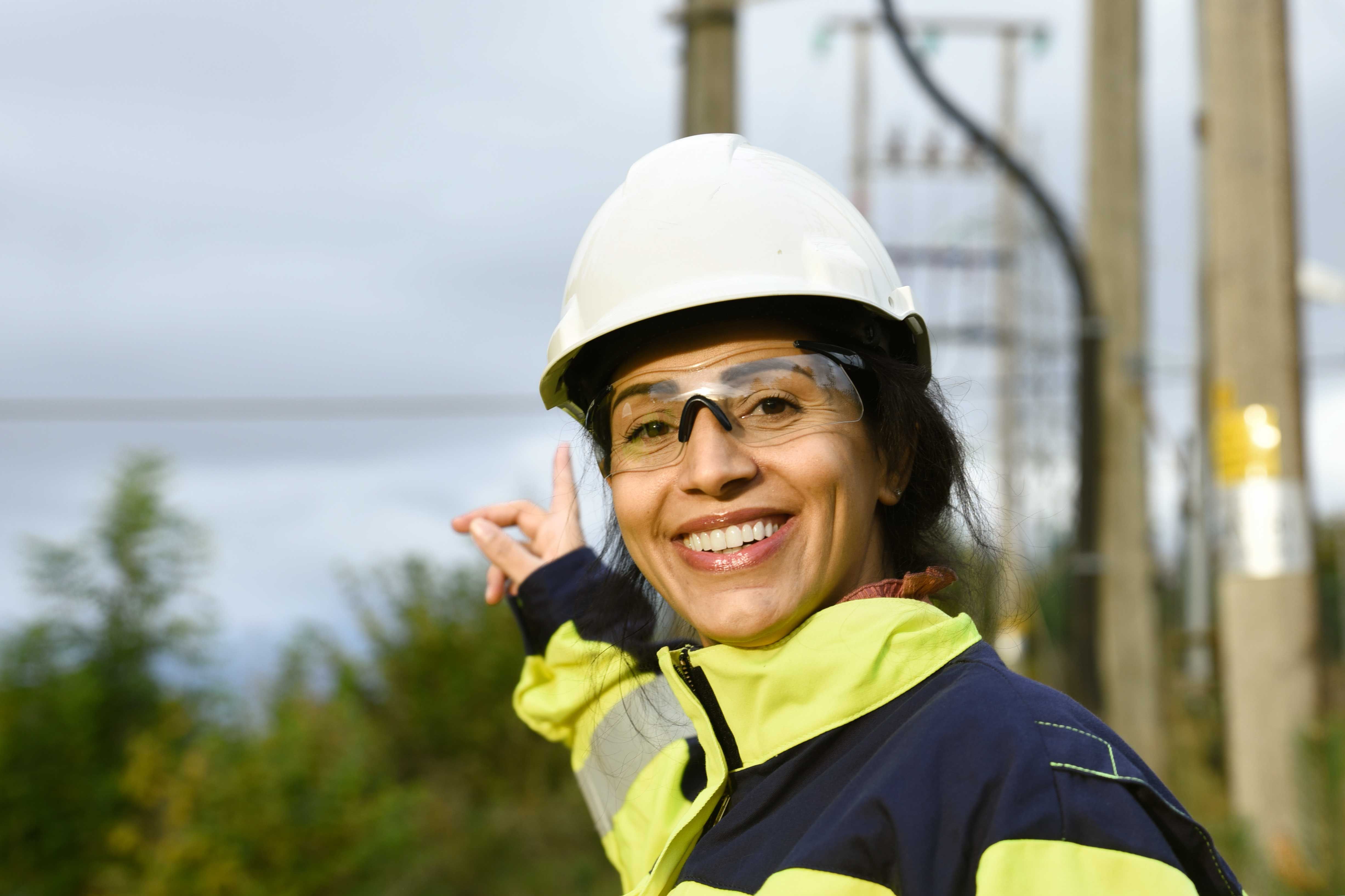 Dame med arbeidstøy og hjelm foran høyspentmast