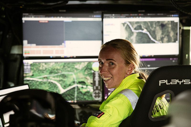 Ung dame med arbeidstøy som sitter foran mange pc skjermer og jobber