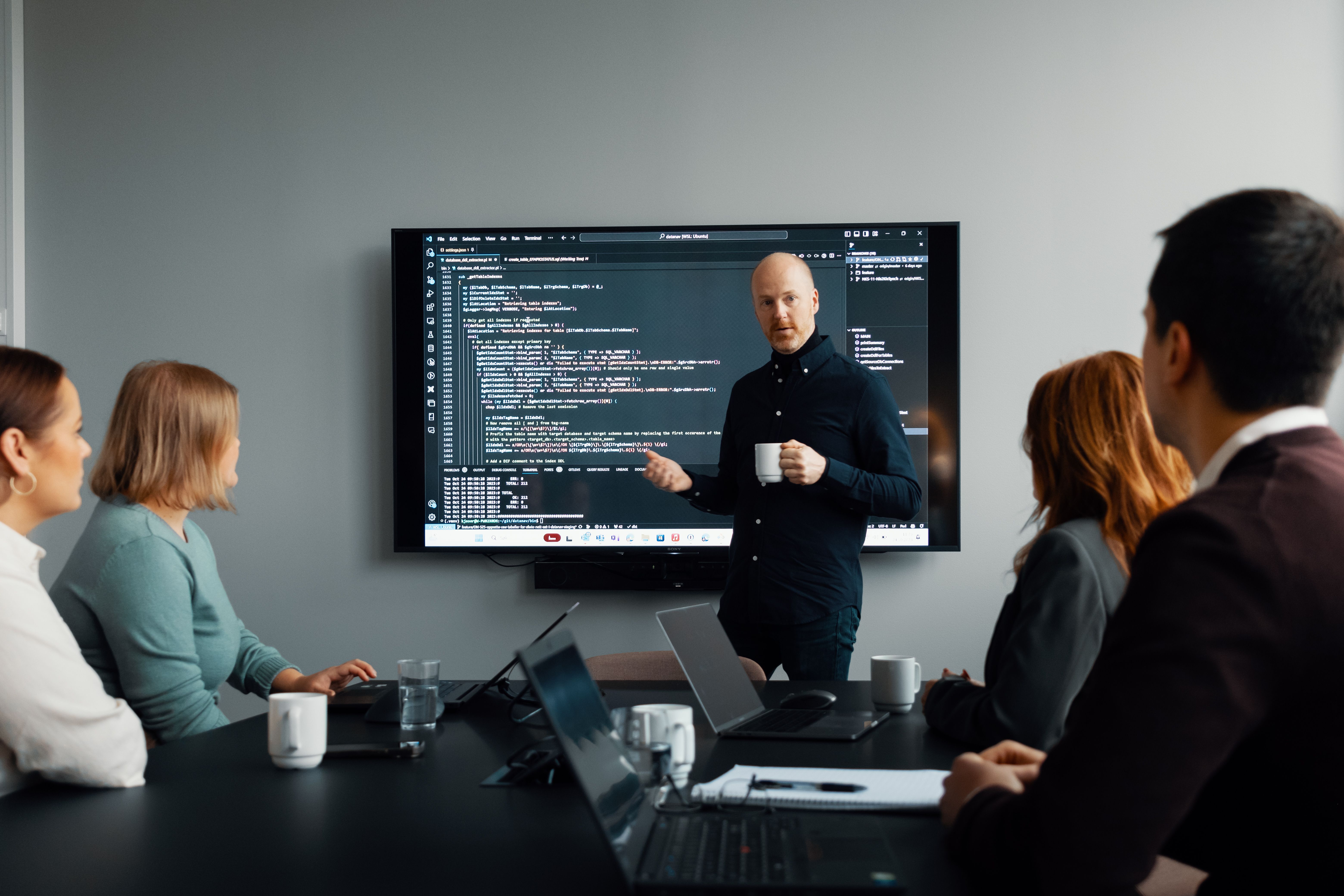 Mann forklarer noe for andre kollegaer foran en skjerm med mye tekst på
