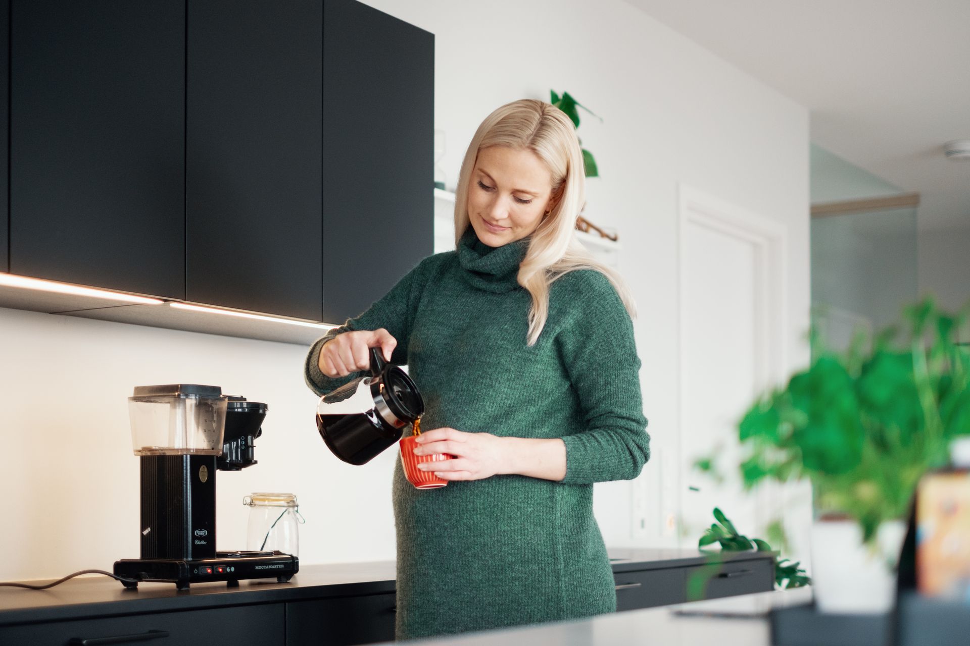 Dame ved kjøkkenbenk som sjenker seg kaffe