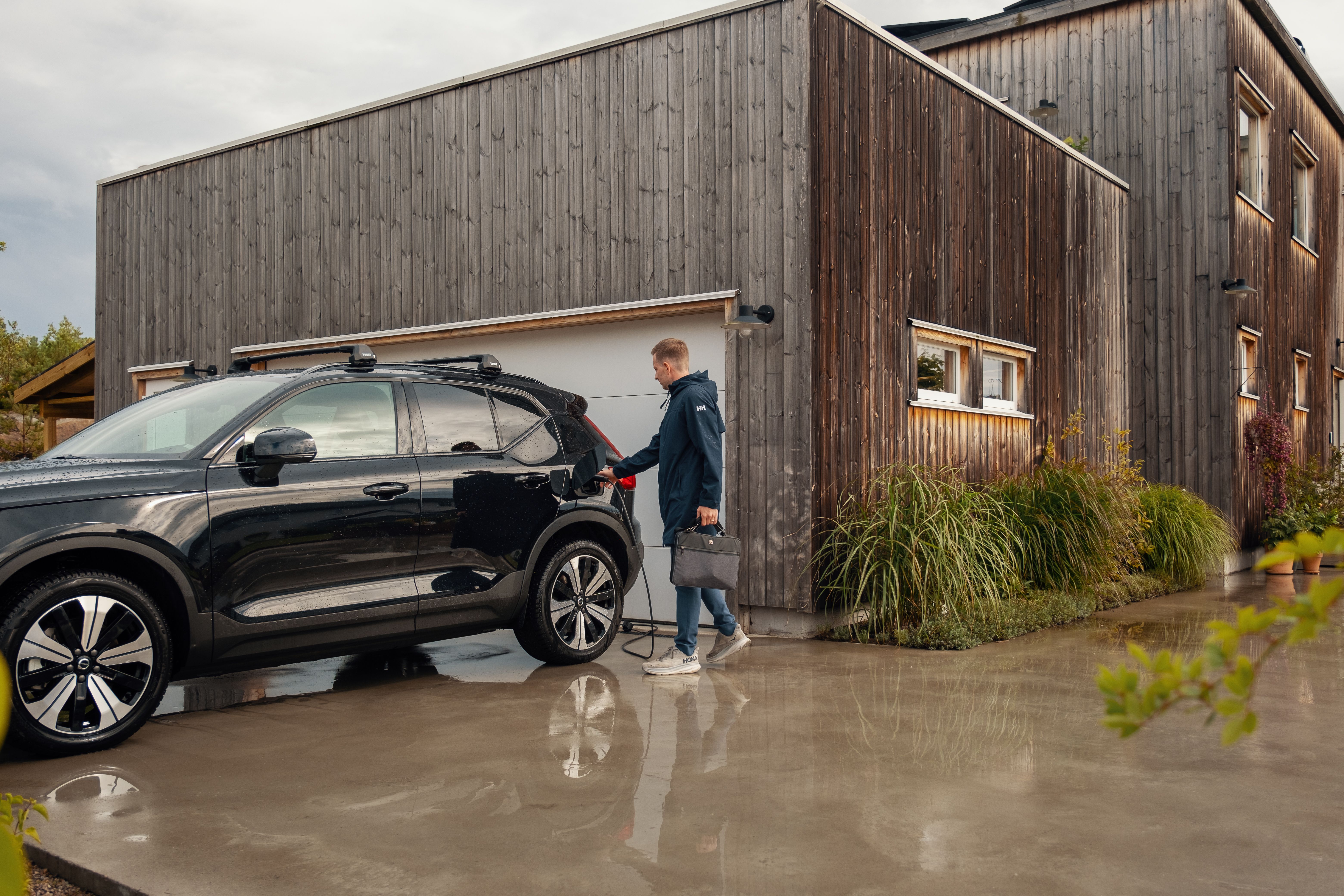 Mann tar ut elbil-laderen av elbilen sin foran huset sitt.