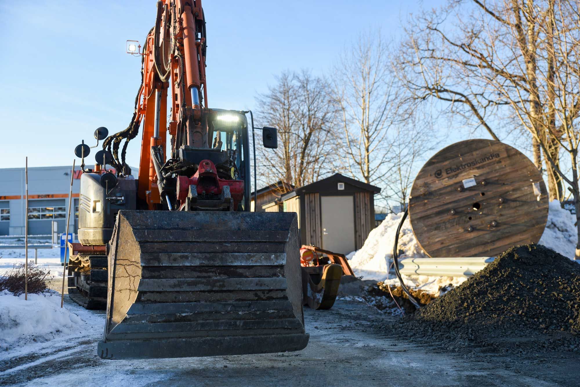 Bilde av en gravemaskin. Blå himmel og snø.