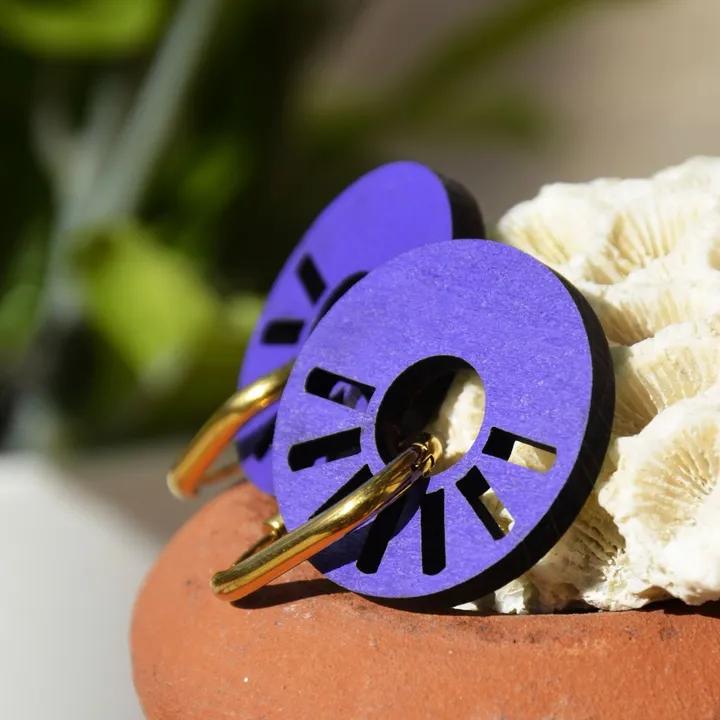 Pendentifs ronds ajourés, violets, sur des anneaux dorés, posés sur un pot en terre cuite