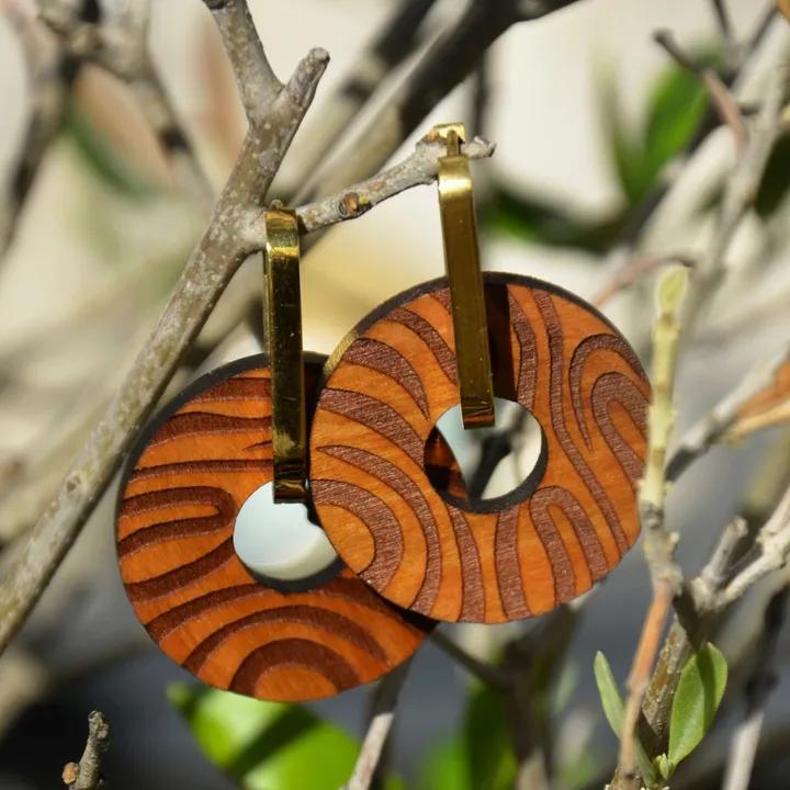 Pendentifs ronds en bois gravé de lignes courbes, sur des attaches dorées, accrochés à une branche d’olivier