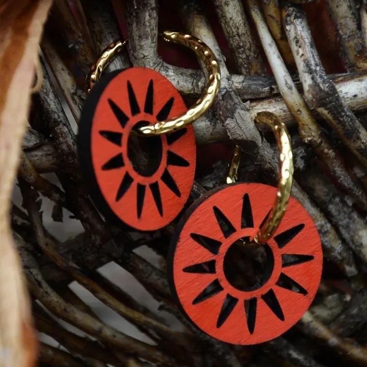 Pendentifs ajourés en rayons, rouges, sur des créoles dorées torsadées, devant un panier en branches