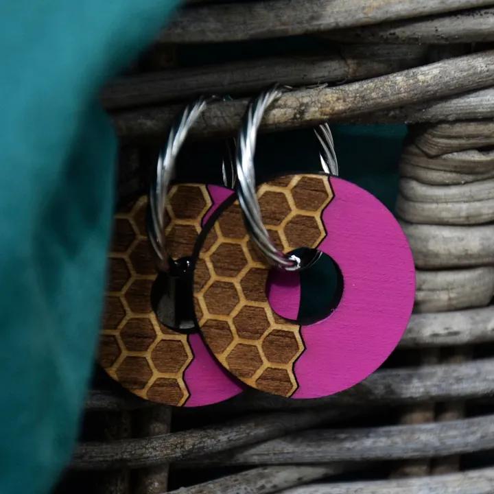 Pendentifs ronds, moitié roses, moitié bois gravé en nid d’abeille, sur des créoles argentées torsadées, devant un panier en osier