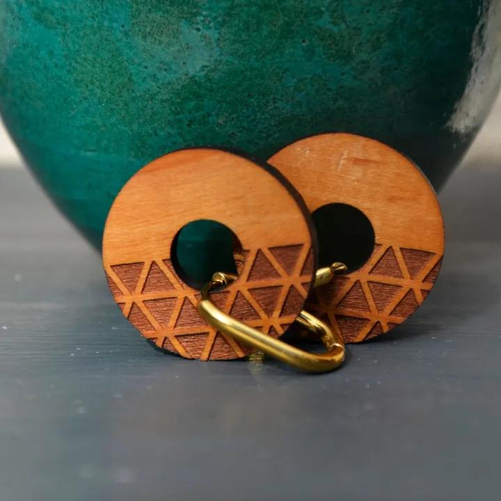 Pendentifs ronds en bois gravé de triangles, sur des anneaux dorés, devant un vase turquoise