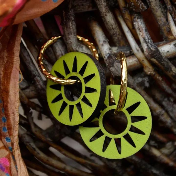 Pendentifs ajourés en rayons, verts, sur des créoles dorées torsadées, devant un panier en branches