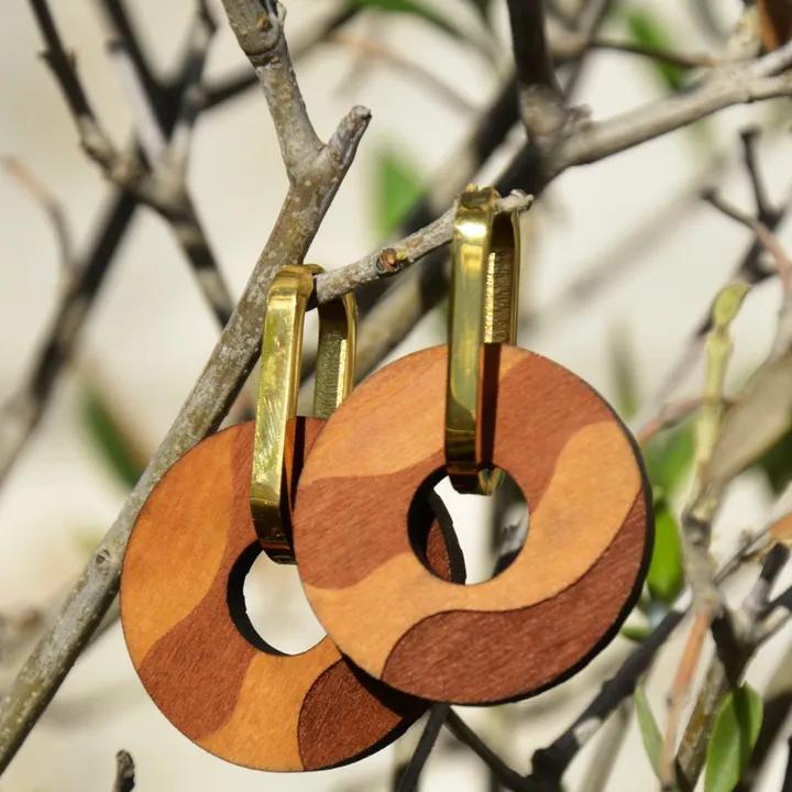 Pendentifs ronds en bois, deux teintes en vagues, sur des attaches dorées, accrochés à une branche d’olivier