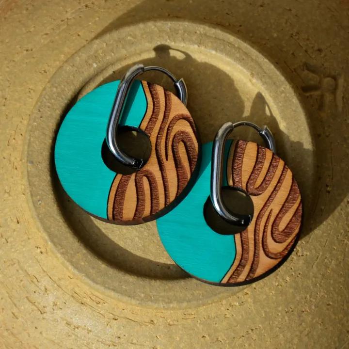 Pendentifs ronds, moitié turquoise, moitié bois gravé de motifs ondulés, sur des créoles argentées, posés sur une assiette en grès