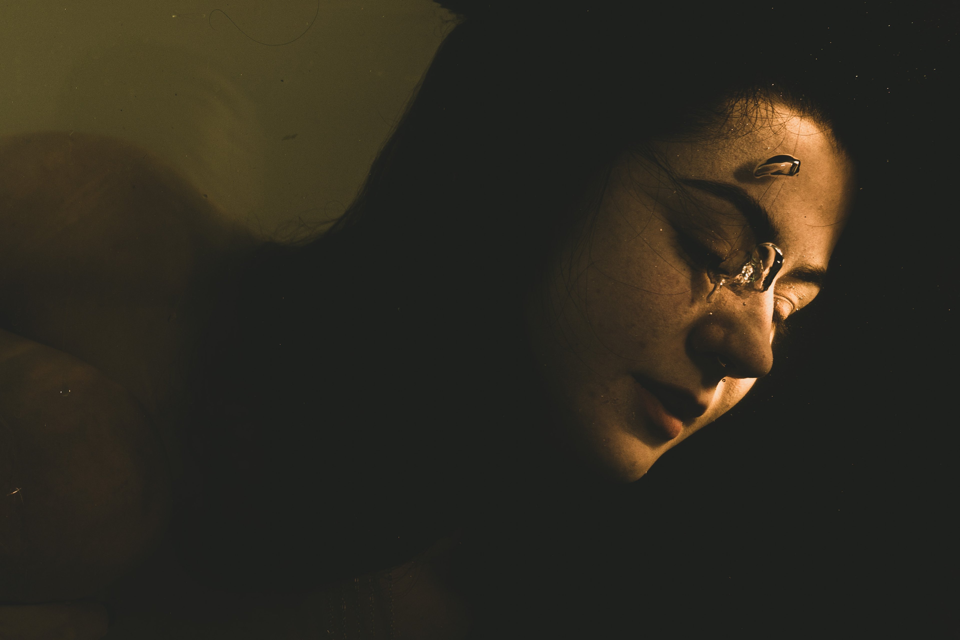 Face at the surface of dark water, lit from one side