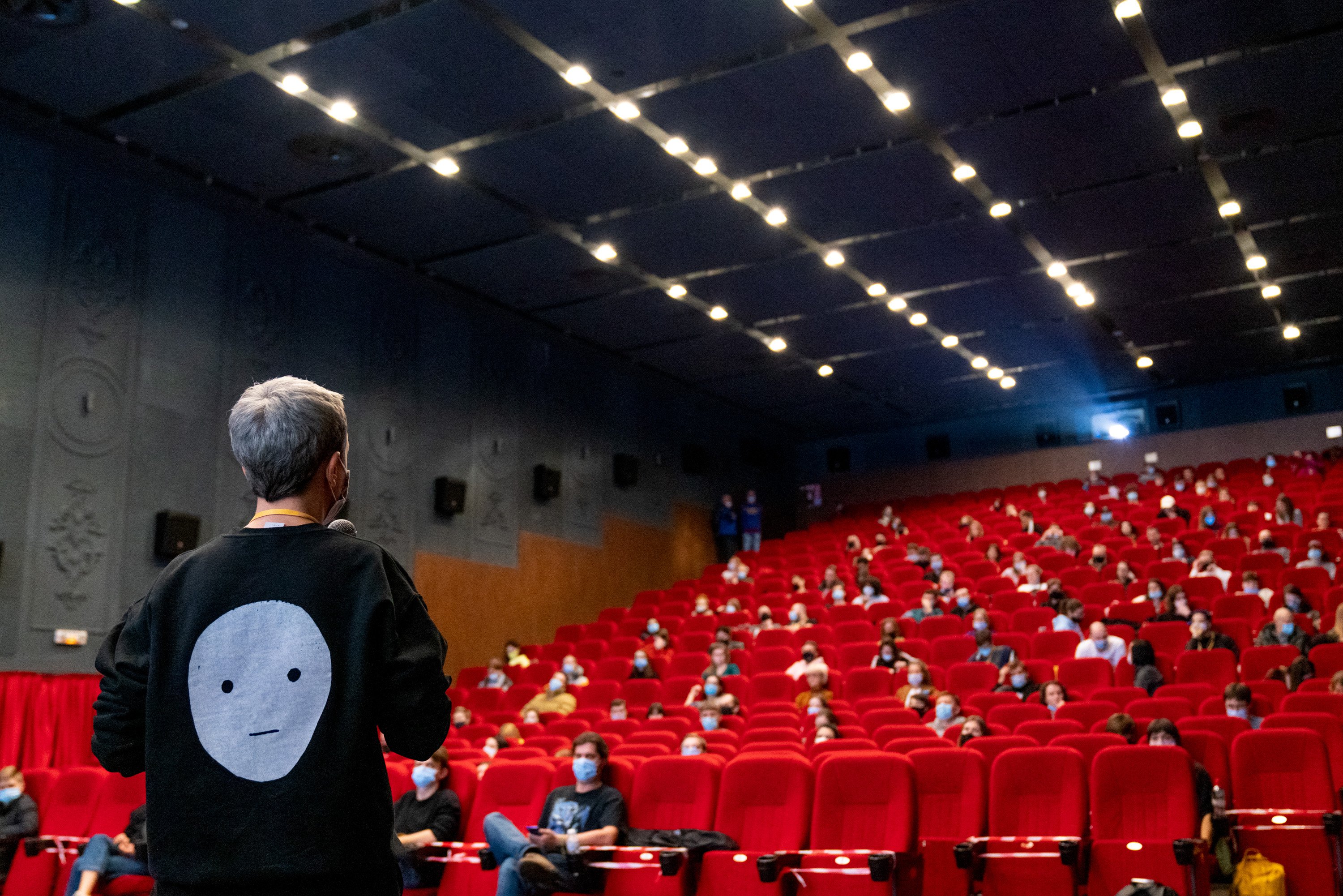 Host addressing a full red-seated cinema hall