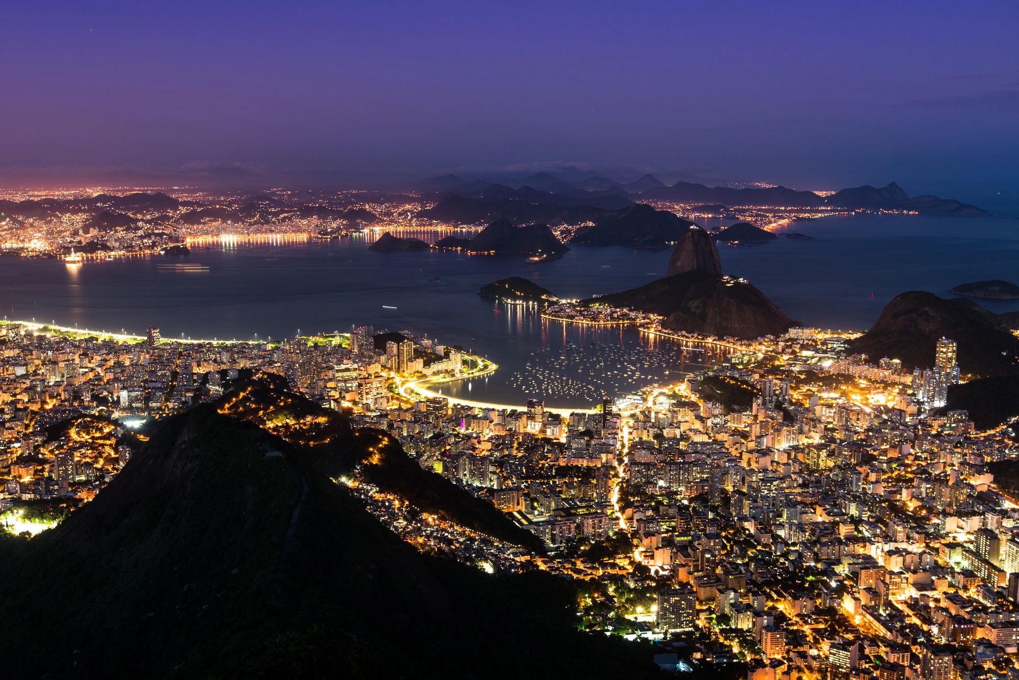 Aerial view of Rio de Janeiro at night with city lights, Sugarloaf Mountain, and Guanabara Bay.