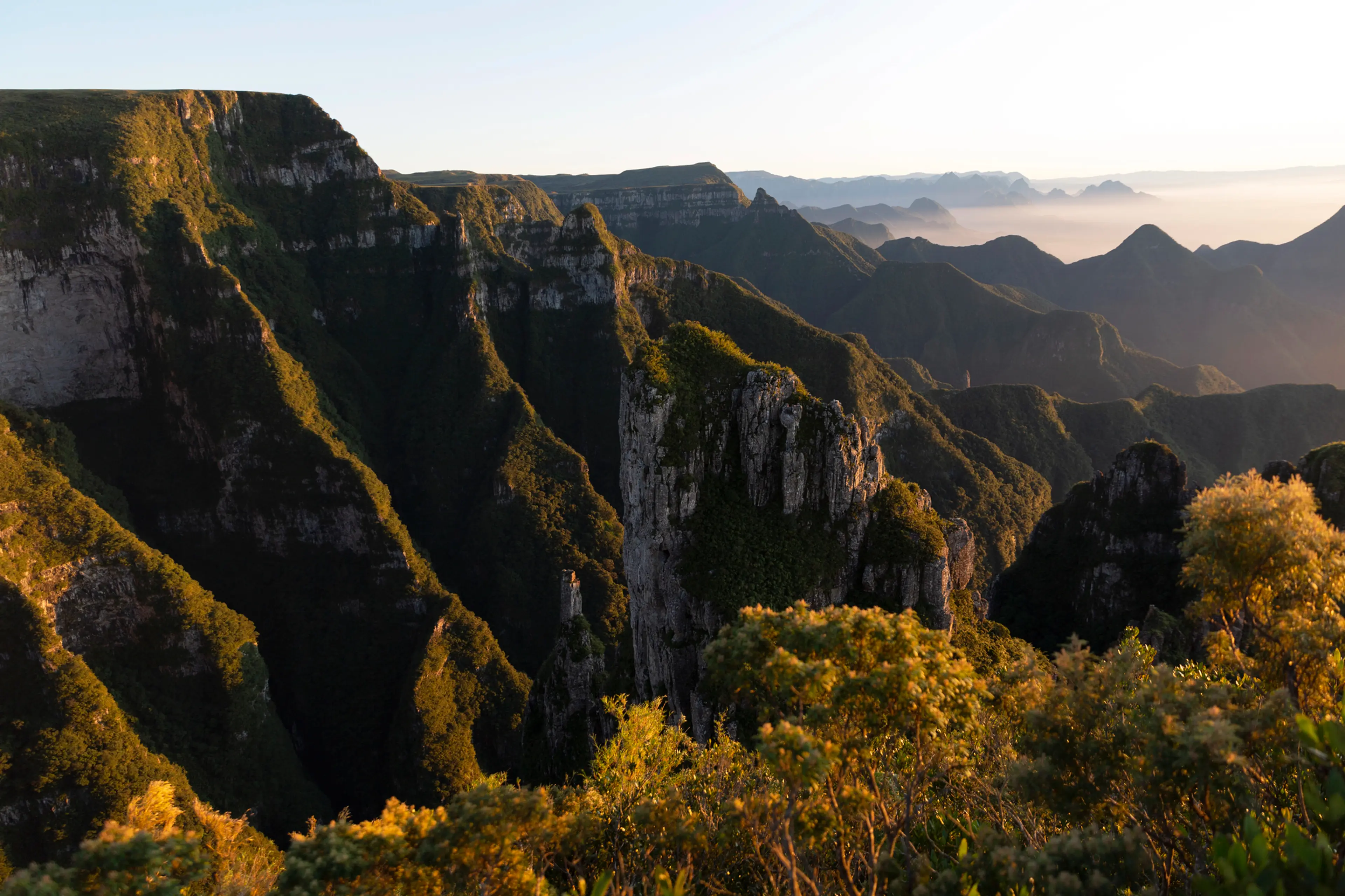 Golden light illuminates a vast mountain canyon with misty peaks in the distance.