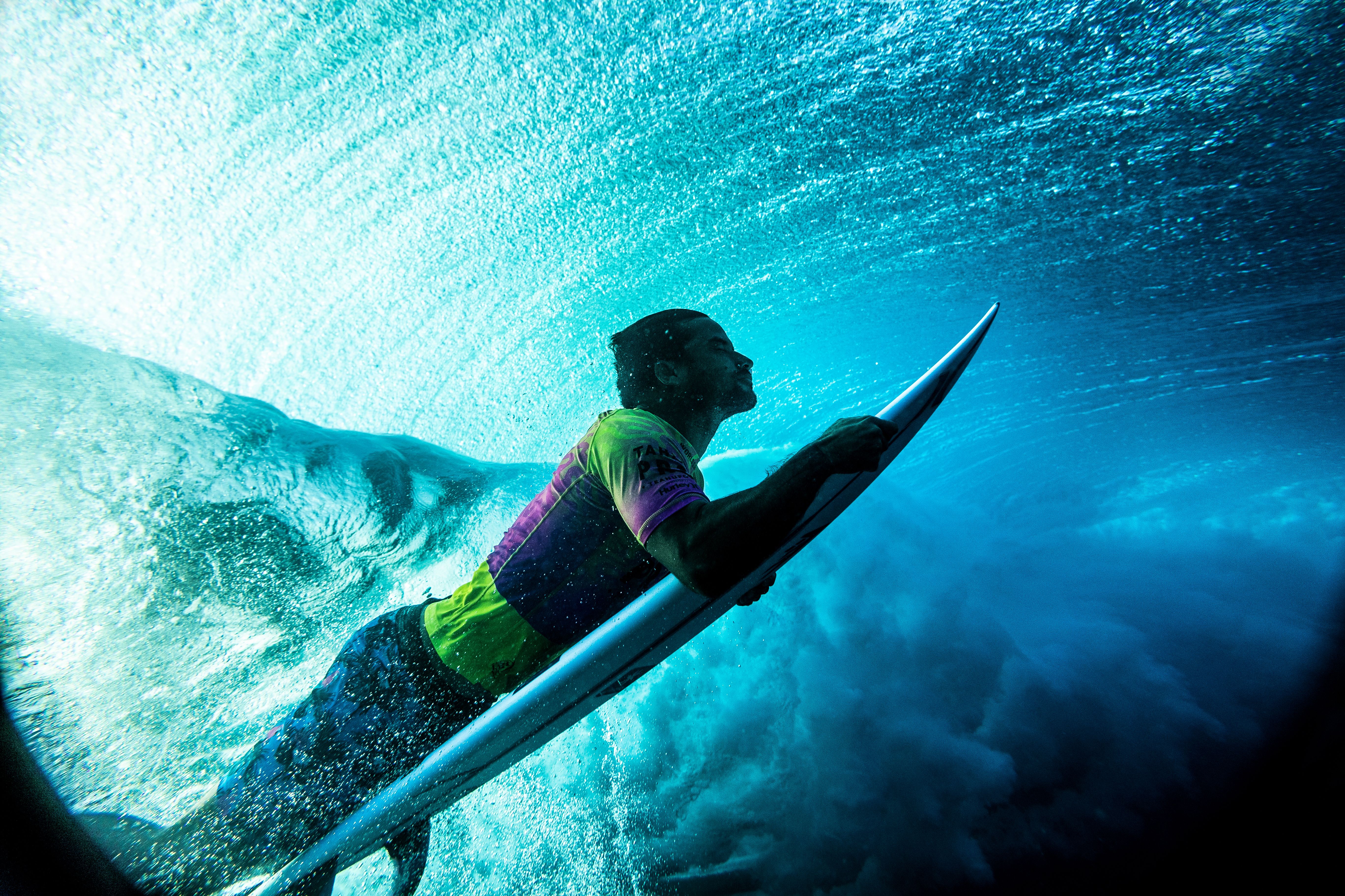 Surfer in a competition jersey duck-diving beneath a breaking wave, shot from underwater