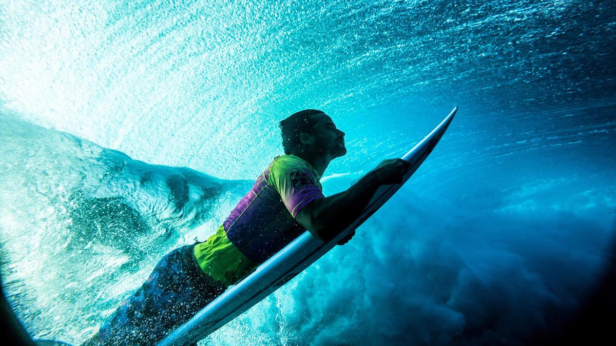 Surfer in a competition jersey duck-diving beneath a breaking wave, shot from underwater