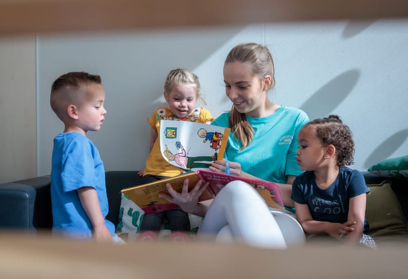 Kinderen lezen een boek samen met de pedagogisch medewerker