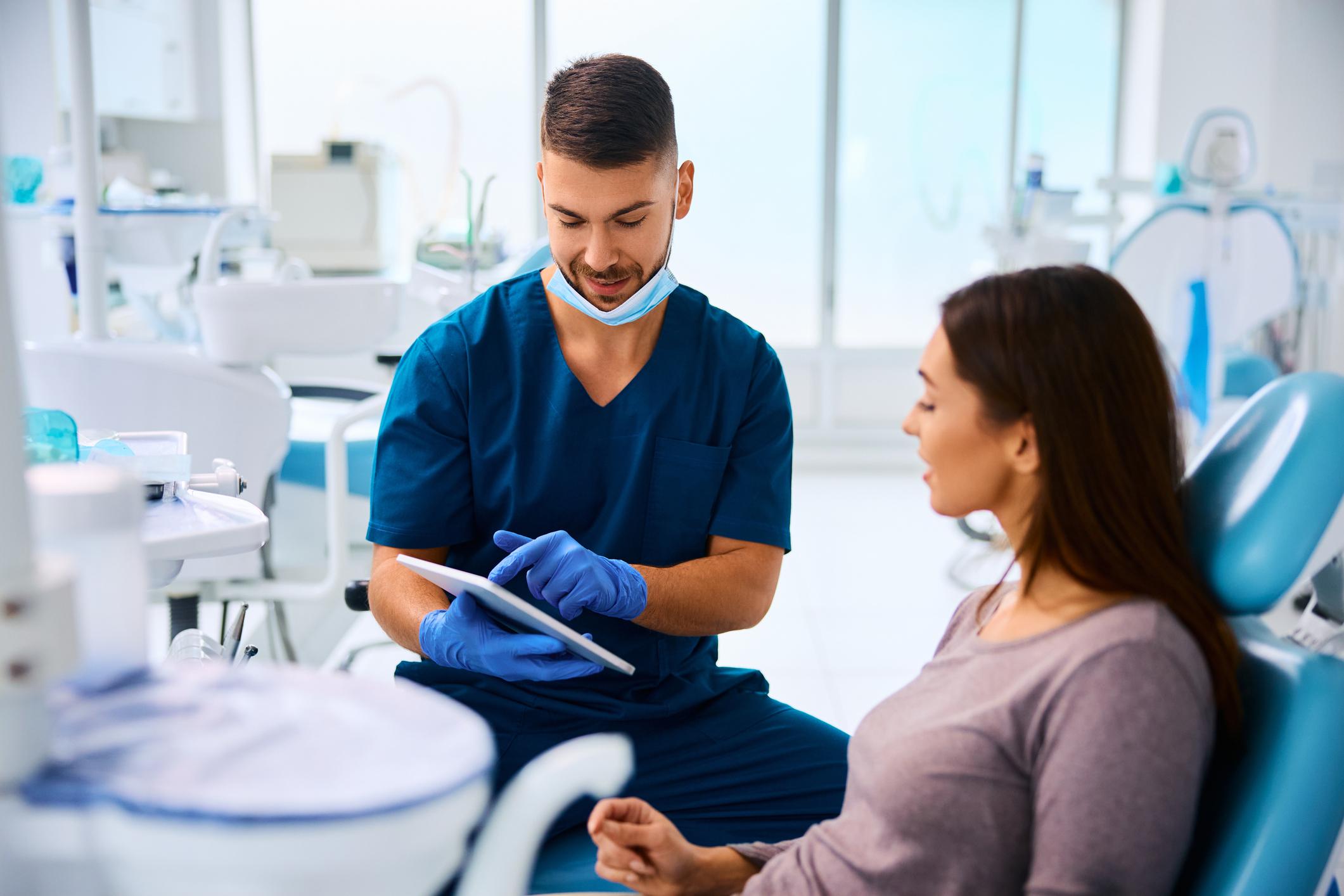 Dental professional reviewing information on a tablet with a patient in a dental exam room.