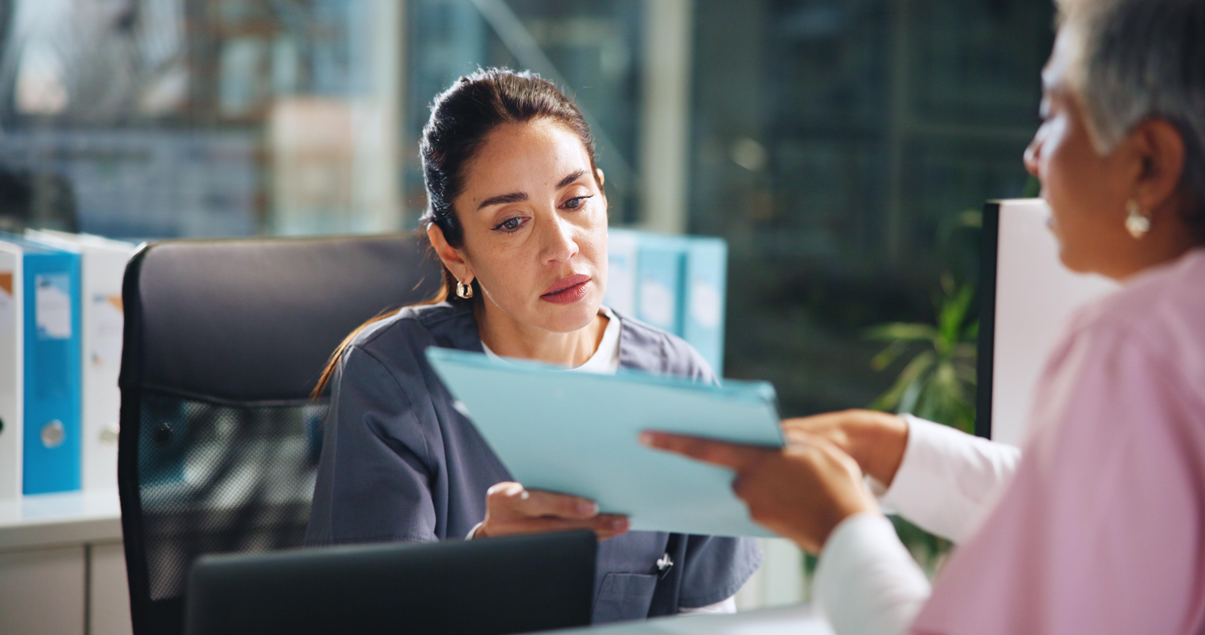 Healthcare staff member reviewing documents with a patient in an office setting.