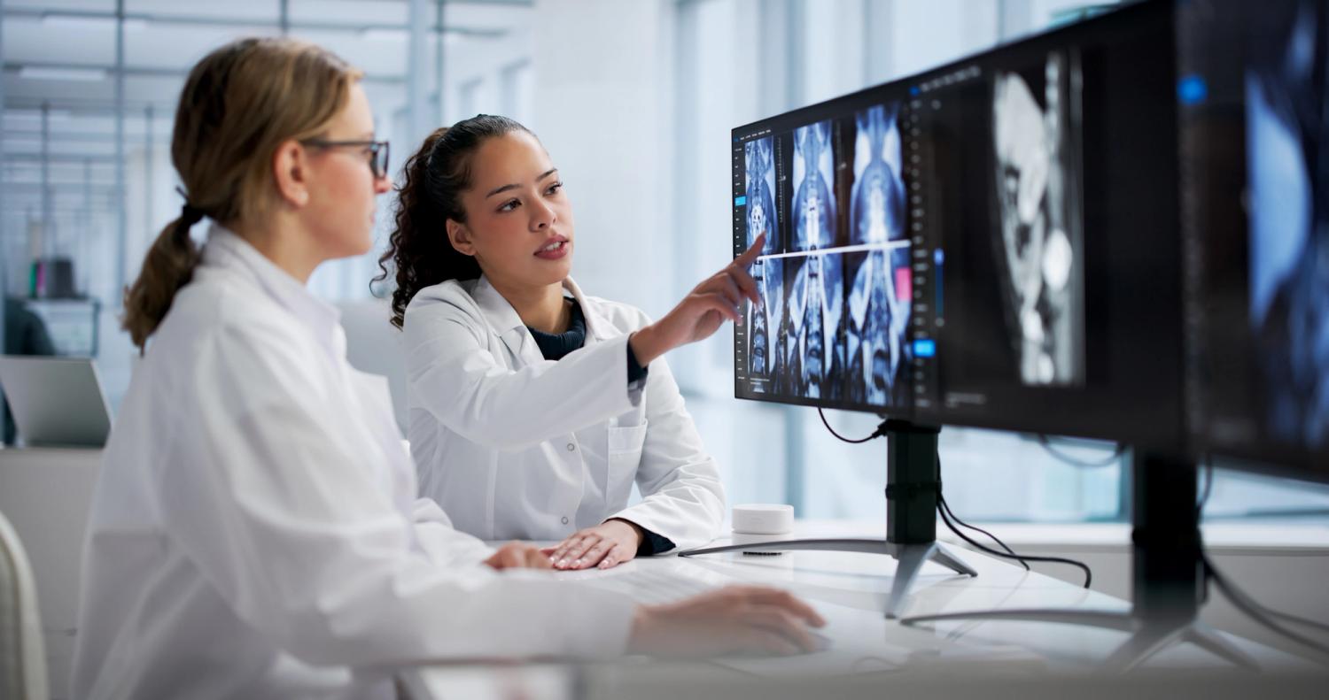 Two radiology specialists reviewing medical imaging on computer monitors.