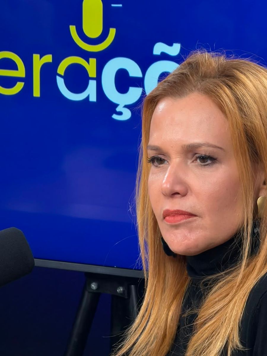 Andrea Eboli falando durante gravação, com o painel do Gerações Cast ao fundo