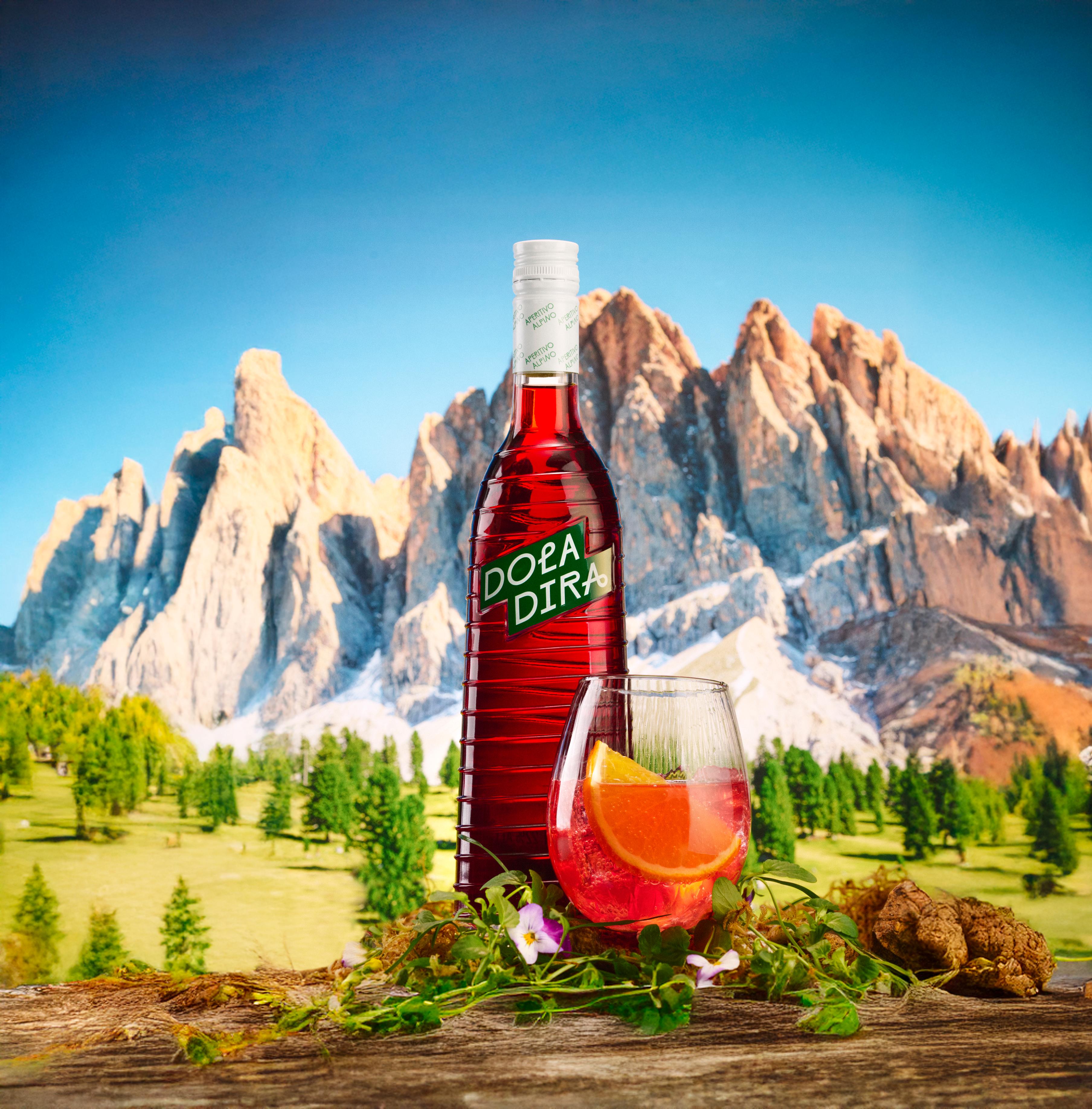 Doladira bottle with the Dolomite cocktail next to it, in front of the Dolomite mountains