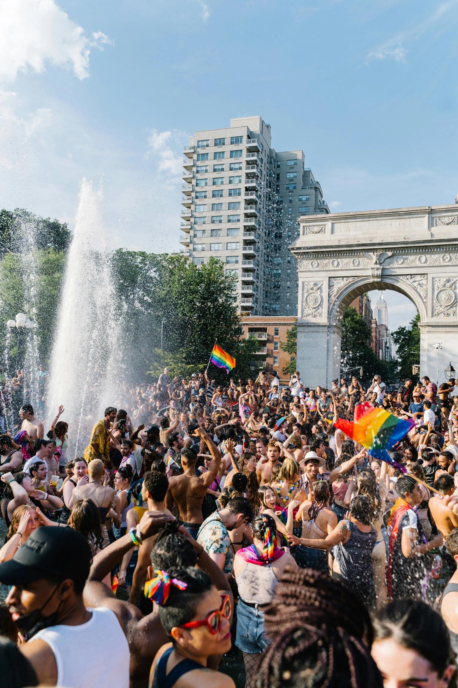 A jubilant summer crowd celebrating around the fountain and arch in Washington Square Park