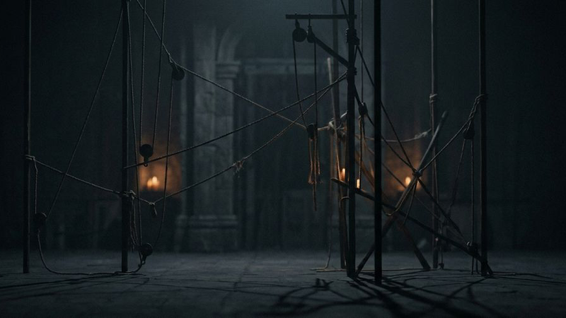 A man stands in a dimly lit elevator with closed doors. A subtle orange glow highlights muted gray walls, creating a mysterious atmosphere.