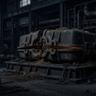 A dark, atmospheric industrial workshop containing a large, heavily weathered metal machine component resting on a steel platform, surrounded by chains, pipes, machinery, and scattered industrial debris.