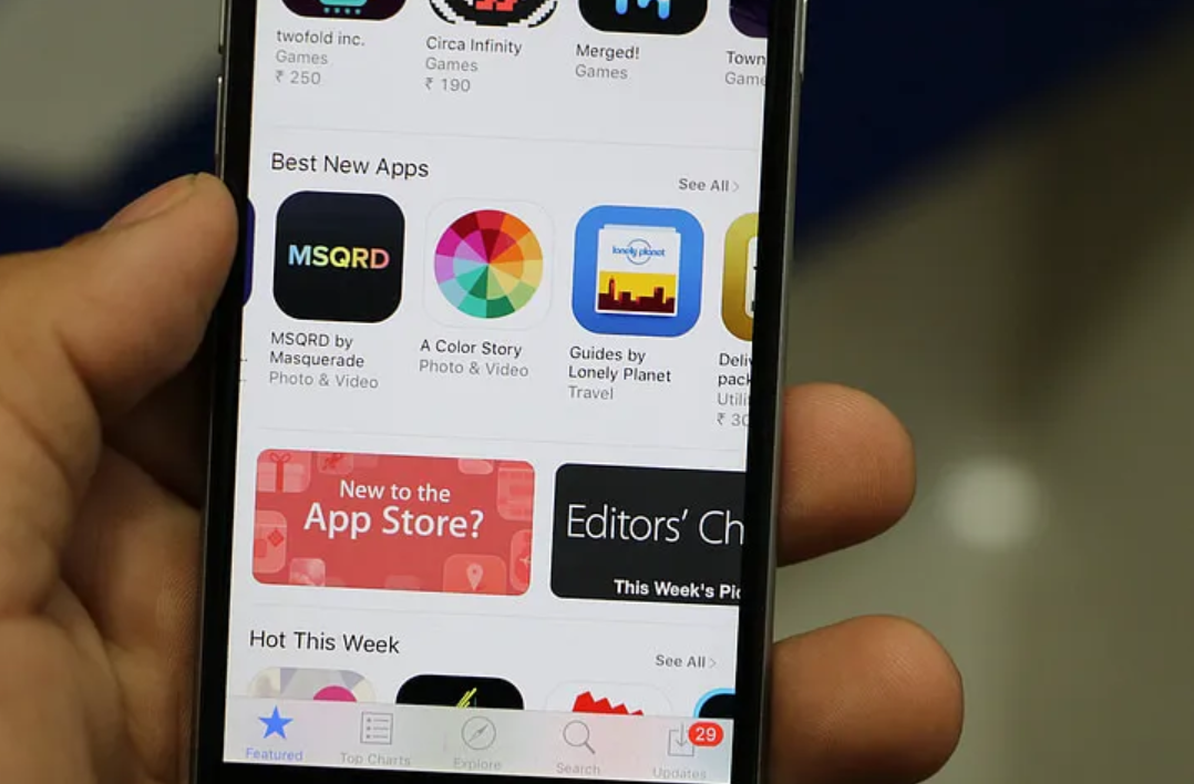 Close-up of a hand holding a smartphone displaying app icons and text like "New to the App Store?" and "Editors’ Choice." Bright screen.