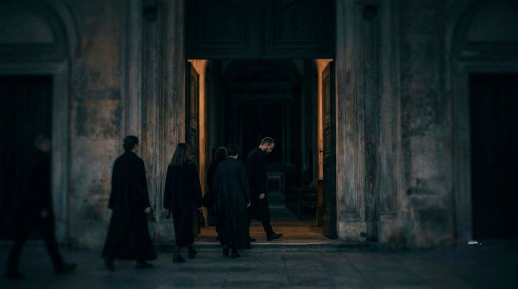 A dark, minimalist scene showing a glowing, arched doorway with a shadowy figure standing inside, partially reflected on a glossy floor, creating a mysterious and atmospheric mood.
