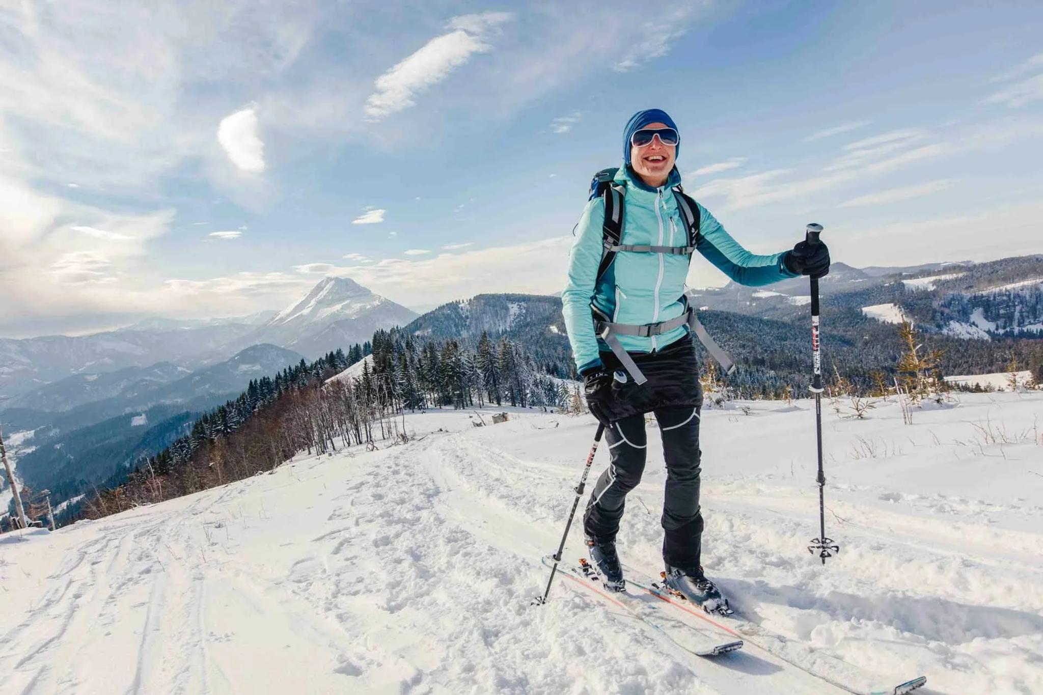 Eine Frau besteigt mit den Tourenski bei wunderschönem Ausblick das Hennesteck