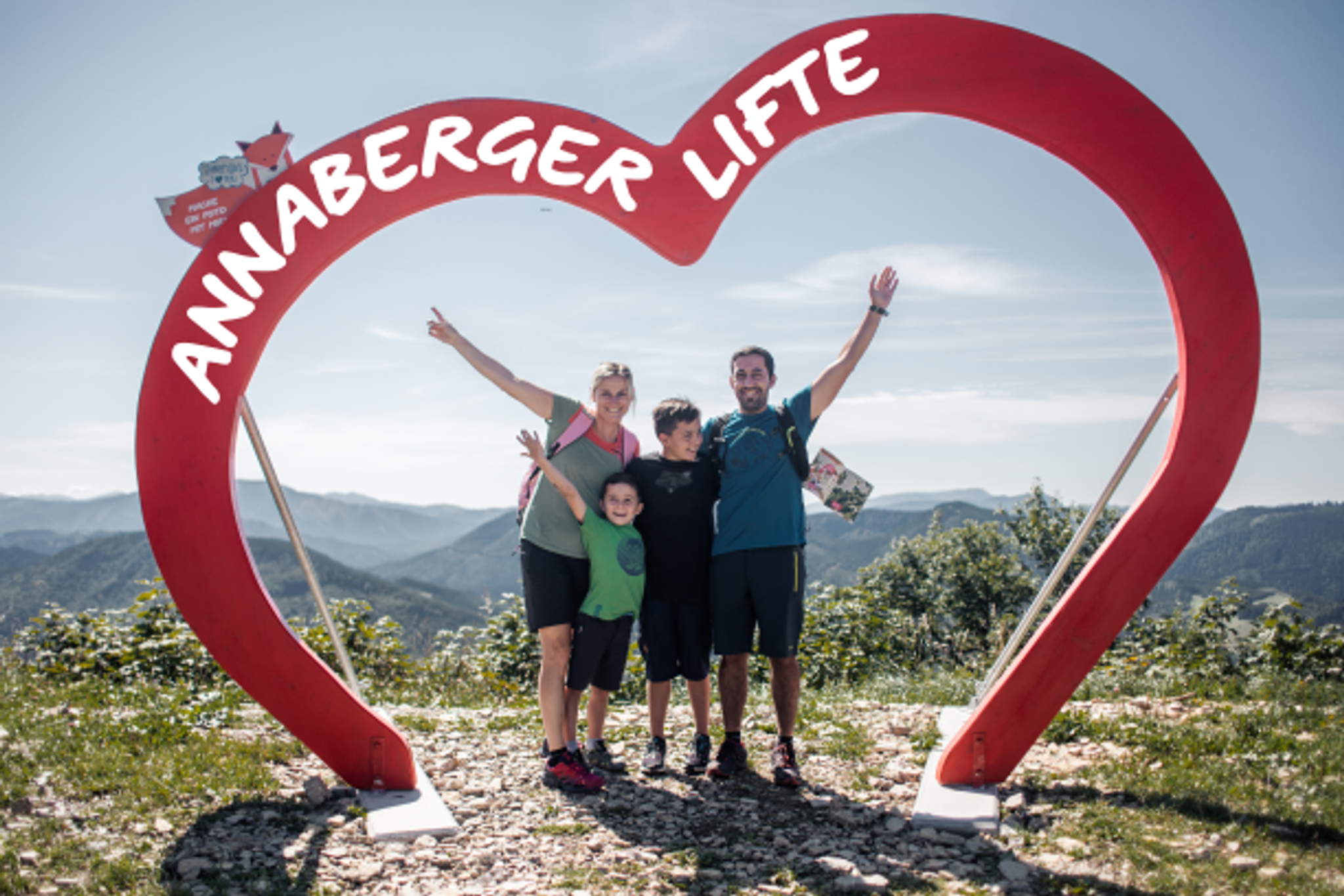 Eine Familie steht glücklich unter dem Fotopoint am Hennesteck, ein rotes Annaberger Lifte Herz