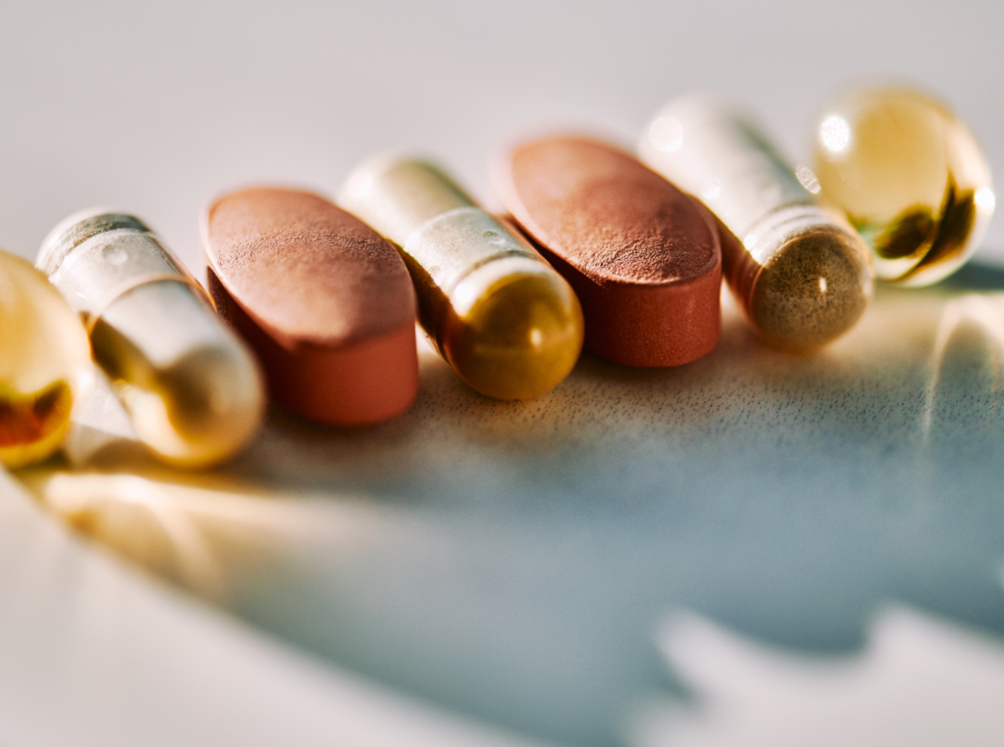 A row of various colorful pills and capsules on a light surface.