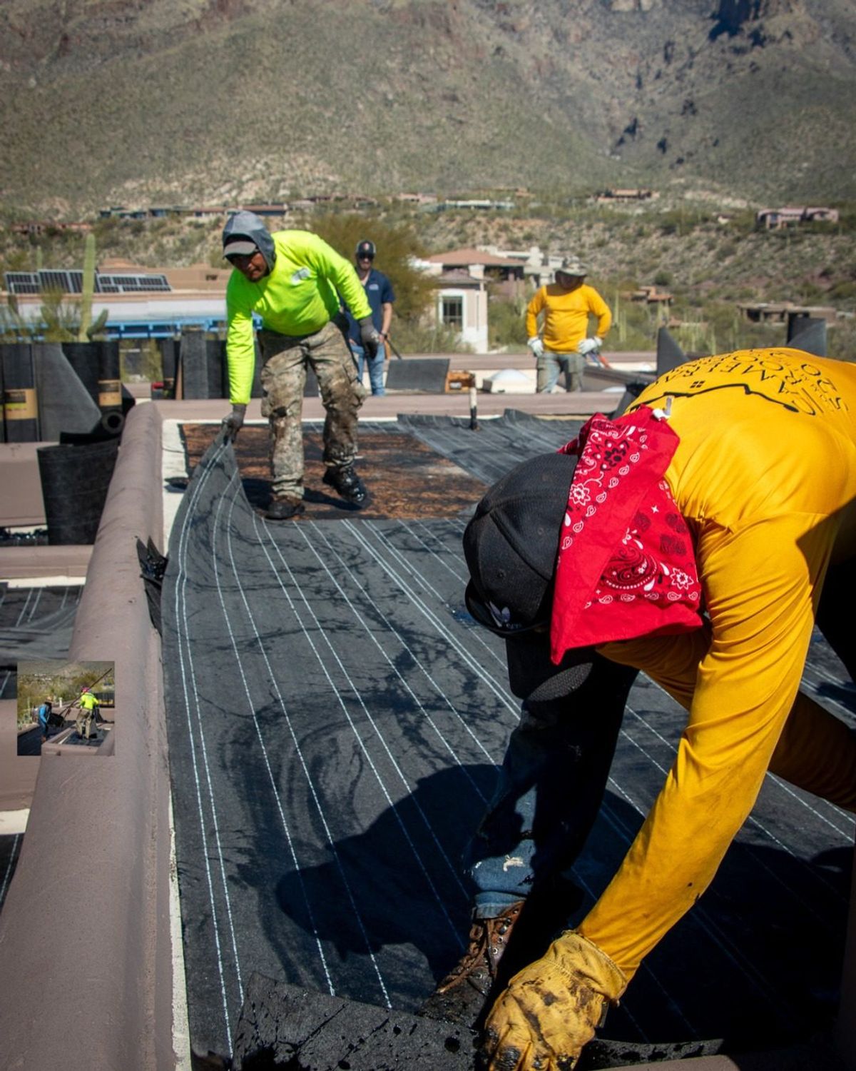 Crew laying down flat roof underlayment, Tucson mountains in the distance