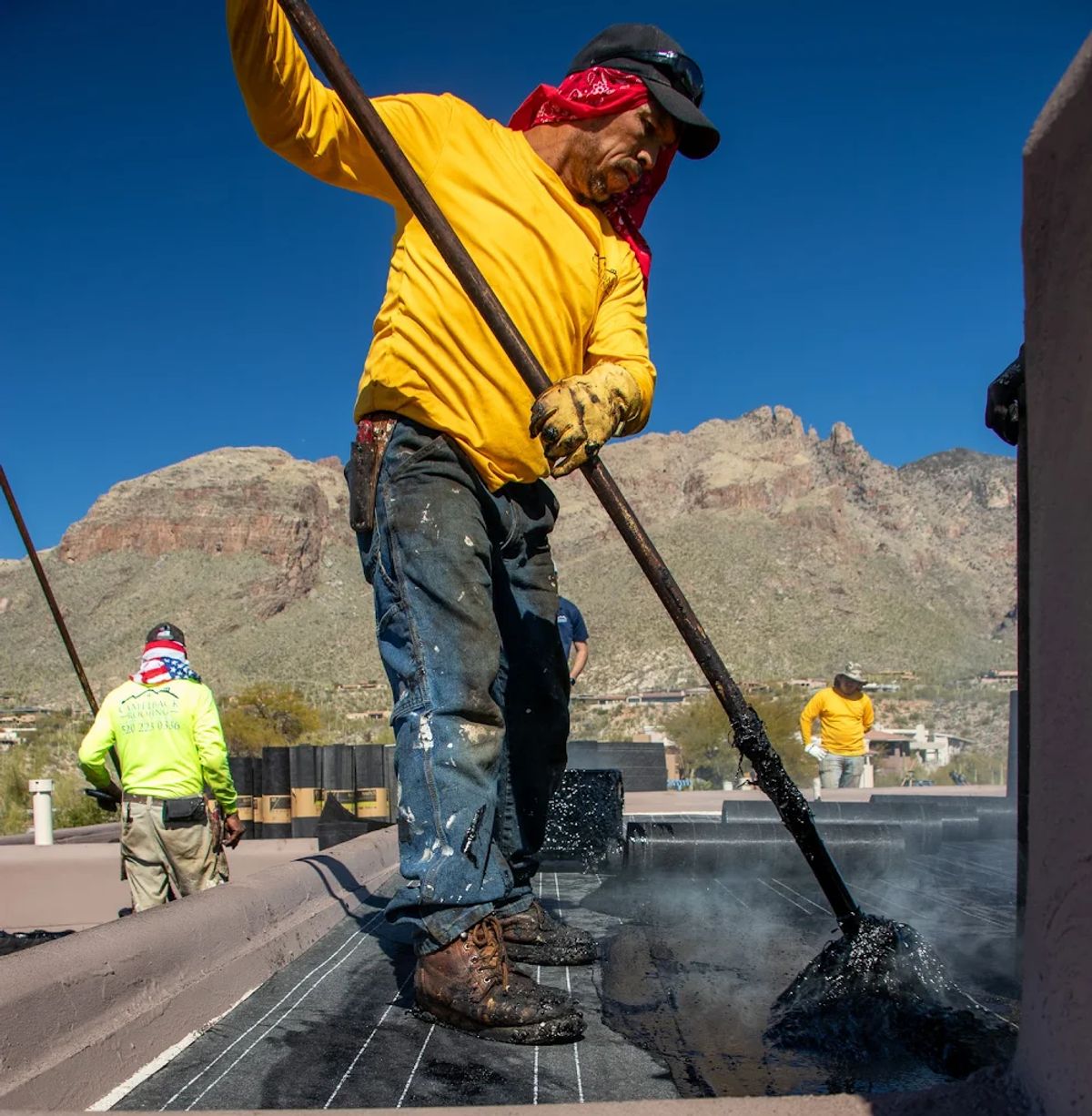Worker in Camelback long-sleeve spreading hot tar on a flat roof