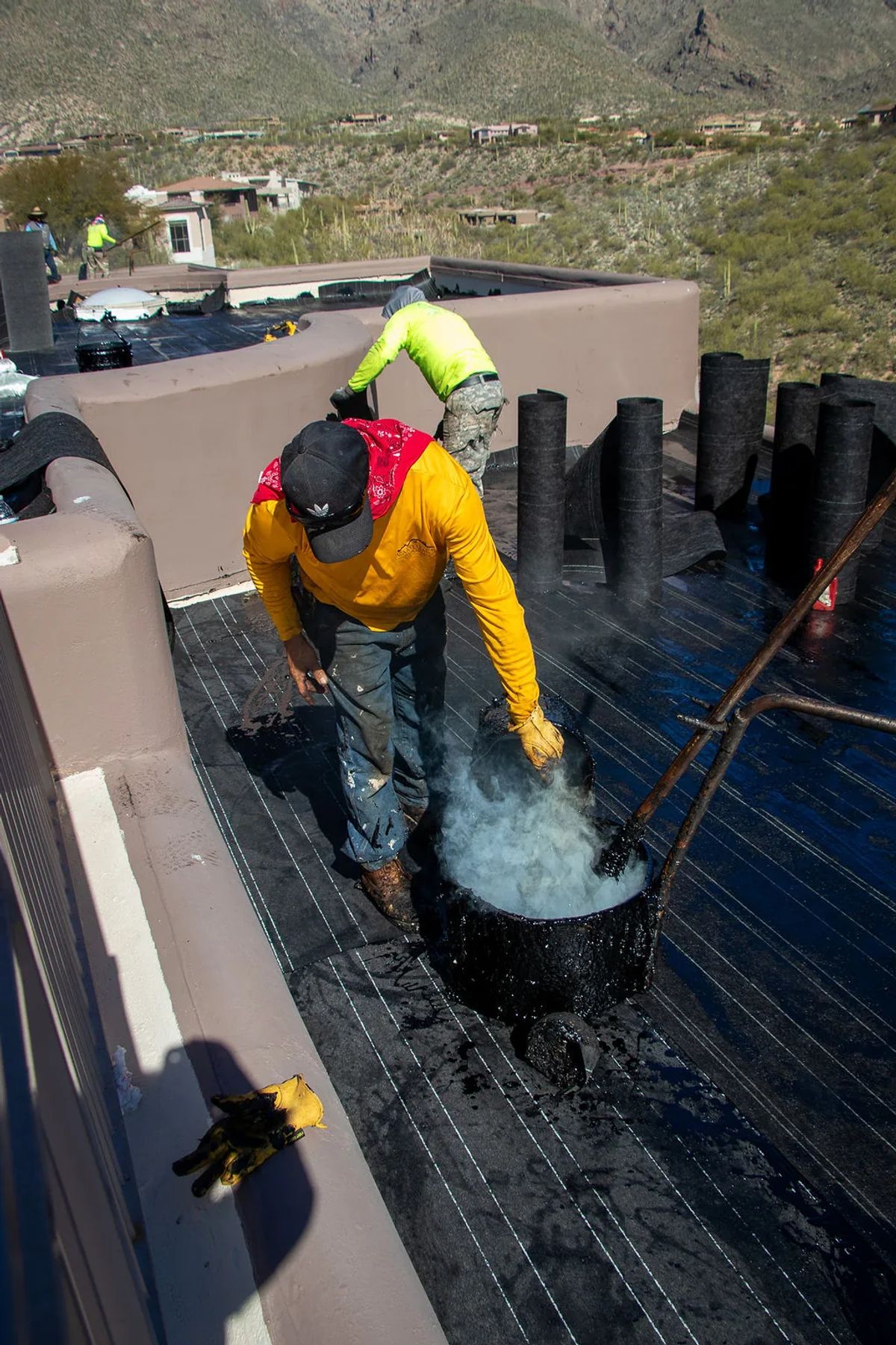 Roofer stirring a bucket of hot tar on a flat roof