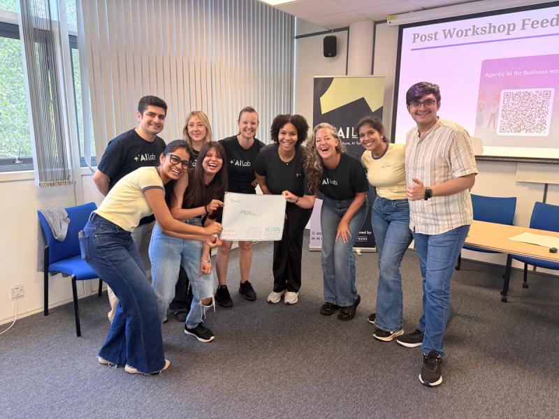 AI Lab facilitators and workshop participants celebrating the completion of an Agentic AI for Business session, several wearing AI Lab-branded t-shirts, AI Lab banner and post-workshop feedback QR code visible in background