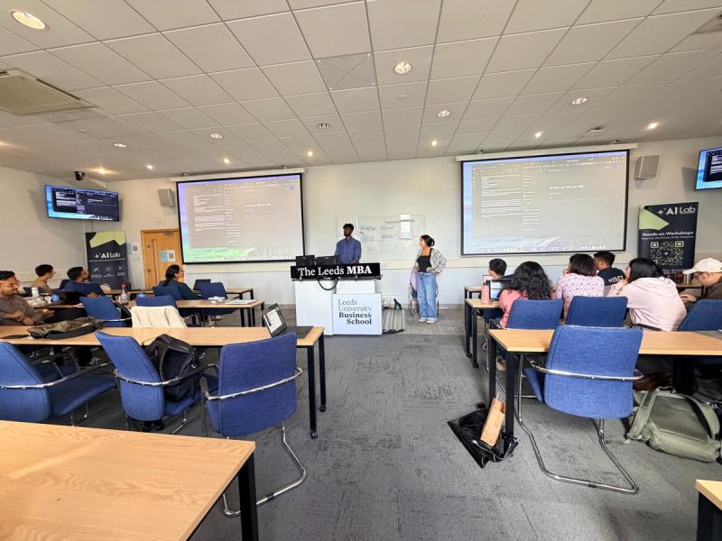 Two presenters at The Leeds MBA lectern with agent output on dual projection screens, Leeds University Business School, 12 June 2026