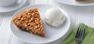 a peanut pie made with chunks of nut next to a ball of ice cream.