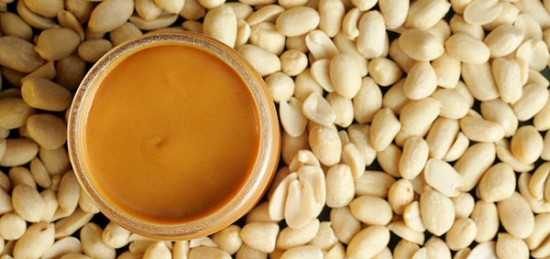 Peanut butter in a bowl surrounded by peanuts.