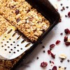 a spoon scooping a square granola bar from a baking tray.
