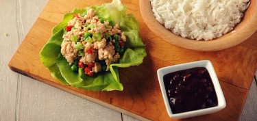 a lettuce leaf filled with meat next to a bowl of rice and a dark sauce.