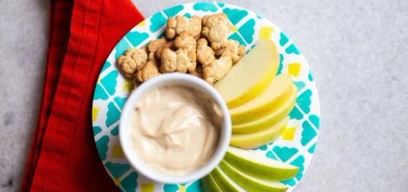 a plate with apples, crackers and a bowl of peanut butter.