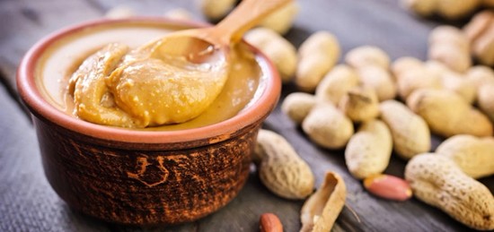 a bowl of peanut butter surrounded by unshelled peanuts.