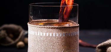 a cocktail drink garnished with a single slice of crispy bacon on top.