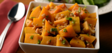 a bowl full of squash chunks topped with green onion and roasted peanuts.